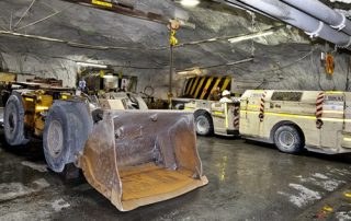 A yellow grader and truck standing in a rocky mine shaft