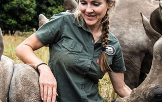 A woman in a green safari shirt placing her hand on rhinos standing on either side of her