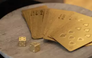 A stack of fanned gold cards and two gold die standing on a small and round wooden table.