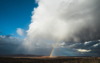 Dark storm clouds over rolling hills with a rainbow extending from it